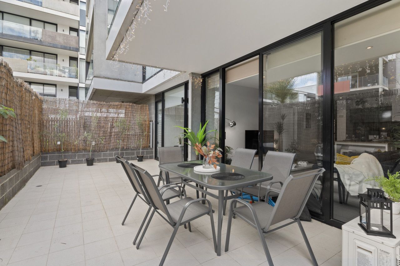 A modern outdoor patio with a dining table and chairs, surrounded by potted plants and a glass enclosure.