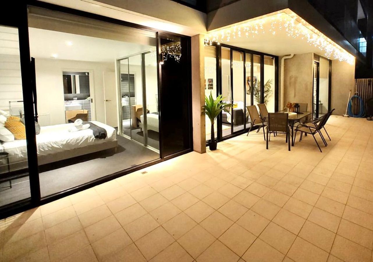 Una habitación de hotel moderna con pared de vidrio, cama y zona de comedor con sillas y mesa.