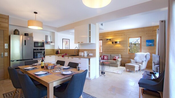 A modern kitchen with a dining area, wooden walls, and a cozy living space with a fireplace.