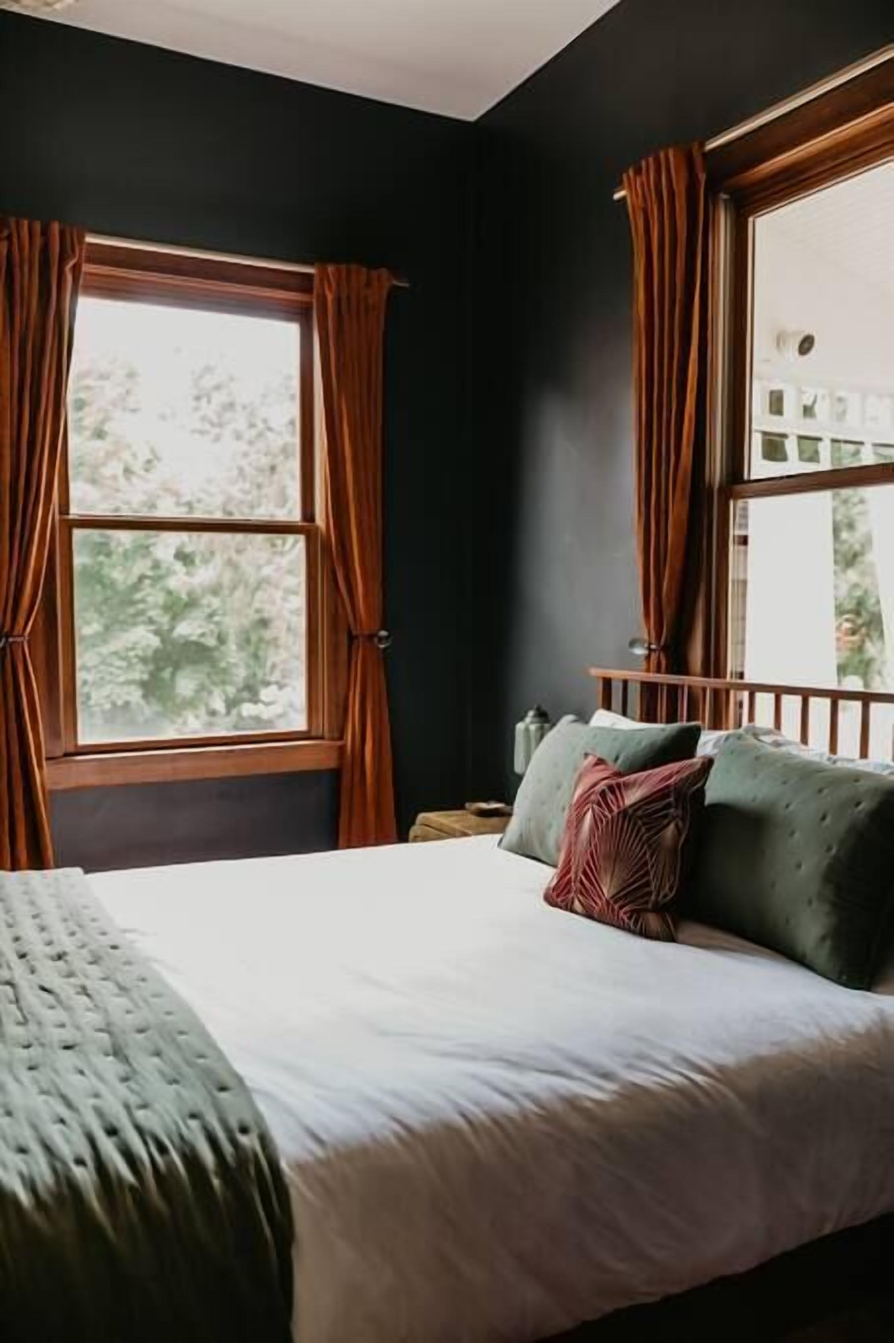 A bedroom with a large bed, dark walls, and a window with curtains.