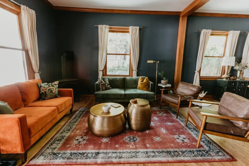 Un salon chaleureux avec un canapé vert, un divan orange et un tapis rouge à motifs.
