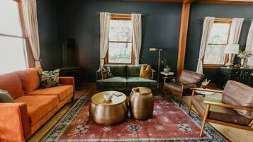 A cozy living room with a green sofa, orange couch, and a red patterned rug.