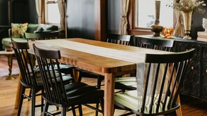 Un comedor con una mesa y sillas de madera, una araña y vistas al exterior a través de amplios ventanales.