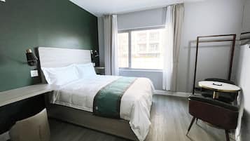A hotel room with a bed, bedside table, chair, and a window with curtains.