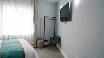 A hotel room with a bed, a TV mounted on the wall, a chair, and a window with curtains.