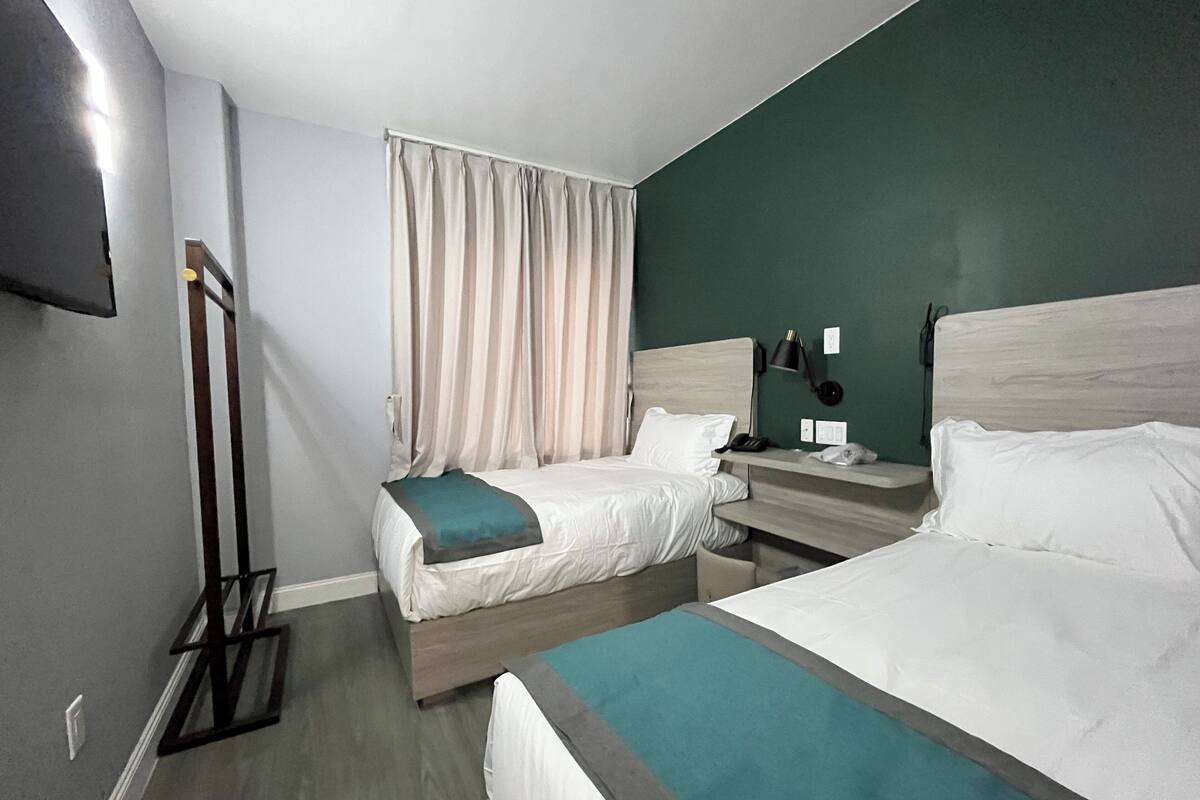 Hotellihuone, jossa on kaksi sänkyä, televisio, yöpöytä lampun kanssa ja ikkuna, jossa on verhot.