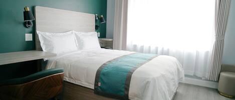 Una habitación de hotel con cama, escritorio, silla y ventana con cortinas.