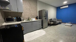 A compact kitchen with grey cabinets, a microwave, a coffee maker, and a refrigerator. There is a grey sofa and a white rug in the living area. - Queen's Two Bedroom apartment with Pool View (Welgelegen)