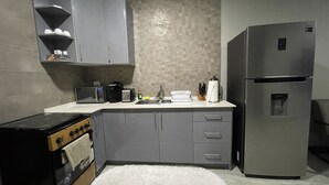 A compact kitchen with grey cabinets, a stainless steel refrigerator, a microwave, and a stove. - Queen's Two Bedroom apartment with Pool View (Welgelegen)