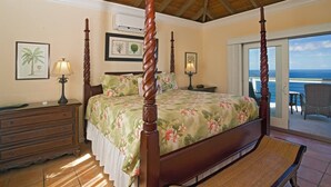 A four-poster bed with a floral bedspread, a wooden dresser, a bench, and a balcony with a view of the ocean. - Oceanfront with Pool, Ocean Views, 5 Bedrooms! (St. Thomas)