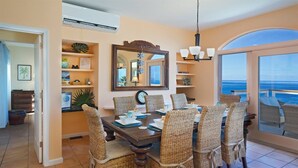 A dining area with a large table and wicker chairs, a mirror above the table, and a view of the ocean through a large window. - Oceanfront with Pool, Ocean Views, 5 Bedrooms! (St. Thomas)