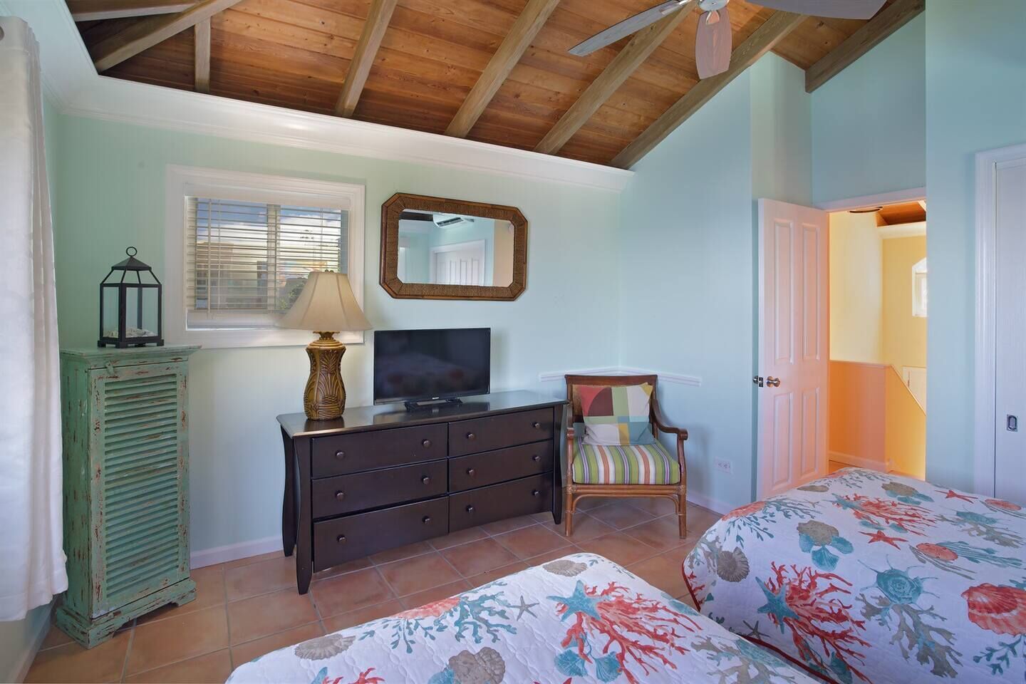 Een slaapkamer met houten plafond, een dressoir, een televisie, een stoel en een bed met bloemenprint beddengoed.