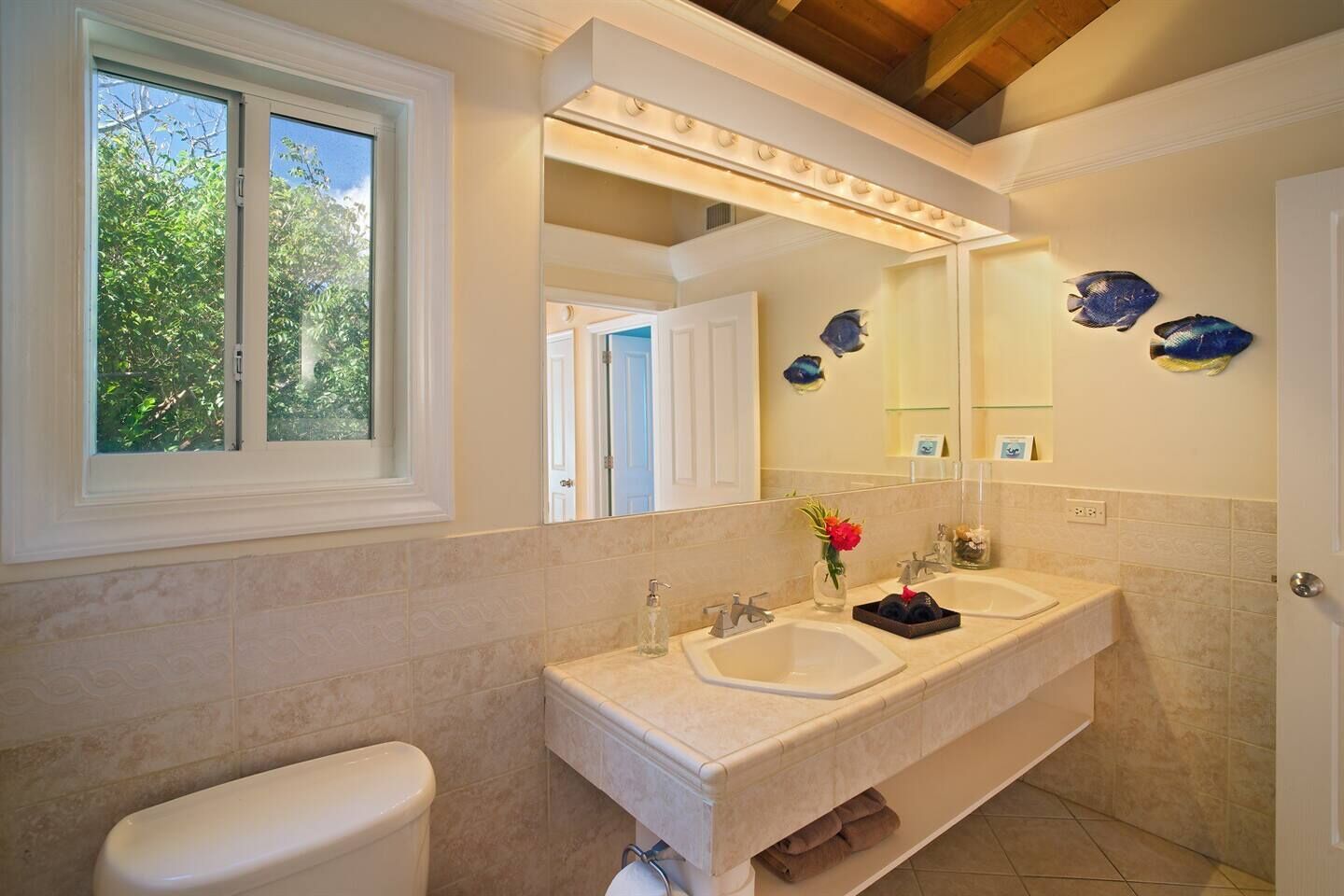 A bathroom with two sinks, a toilet, a window, and decorative fish on the wall.