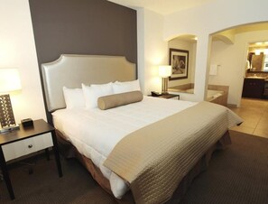 Relax in a spacious room with a large bed, bedside table, and arched doorway to a bathroom with a mirror and sink.
