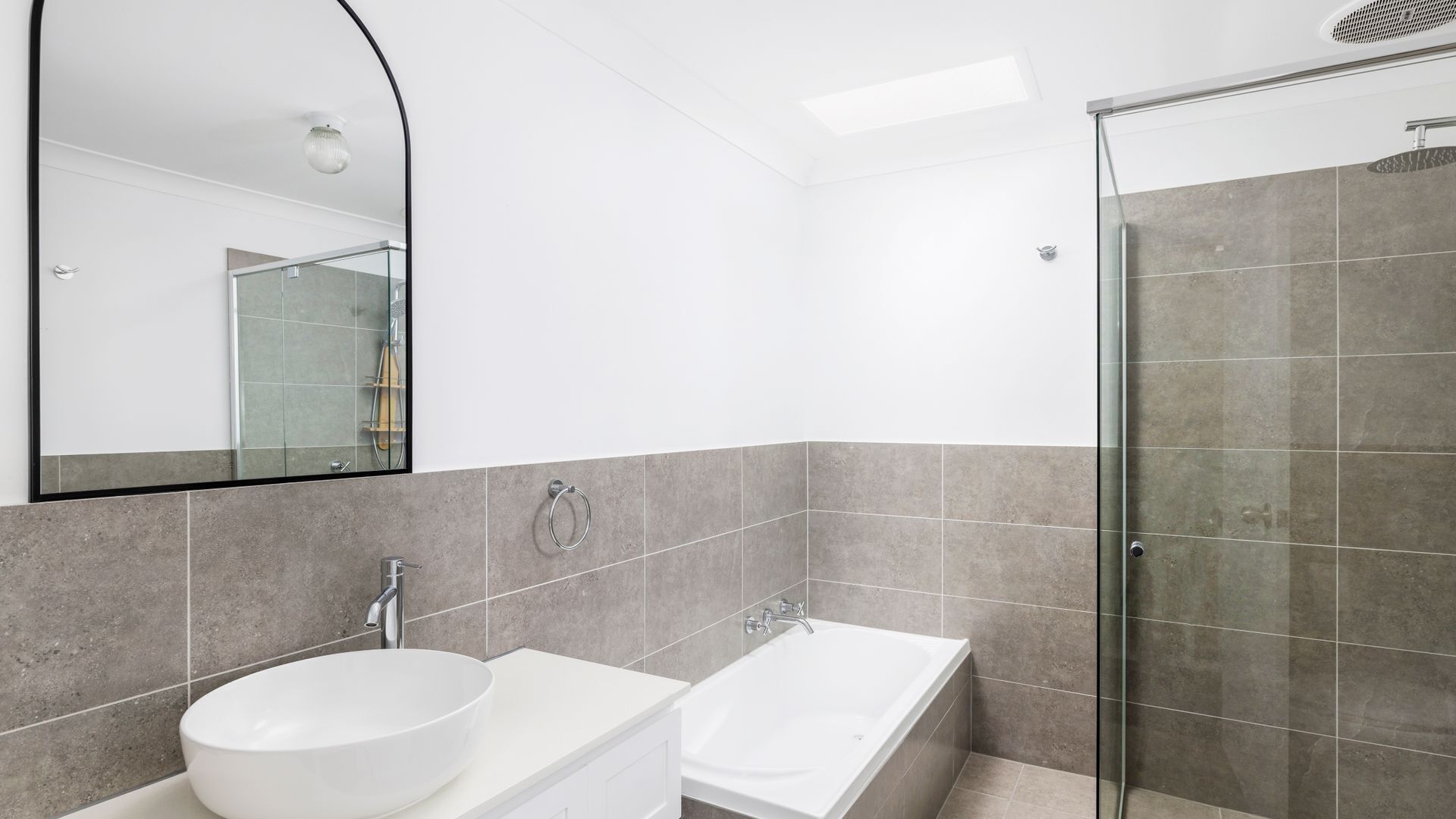 A modern bathroom with a large mirror, a white sink, a bathtub, and a shower area.