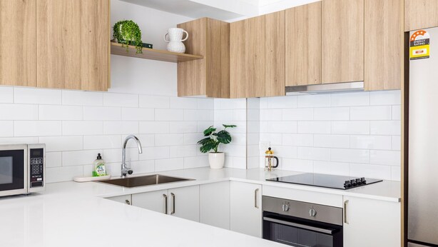 A modern kitchen with white cabinets, a stainless steel sink, a microwave, and an oven.