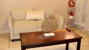 Un salon avec un canapé beige, une table basse en bois, une lampe fixée au mur et une étagère décorative.