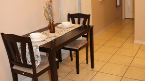 Un coin repas avec une table dressée pour quatre personnes, deux chaises de chaque côté, un vase rempli de fleurs et un élément décoratif fixé au mur.