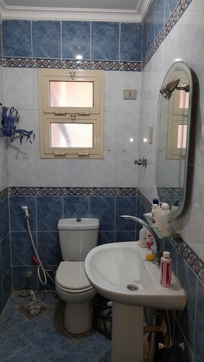 Un baño con azulejos azules, un lavabo blanco, un inodoro y una ventana con marco decorativo.