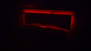 Una habitación oscura con una luz roja que dibuja un rectángulo, posiblemente el marco de una ventana o puerta.
