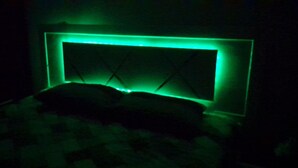 Una habitación tenuemente iluminada con una cama y cabecera bañadas en luz verde.