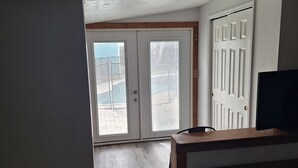 Een kamer met een houten bankje, een witte deur met een raam en een betegelde vloer.