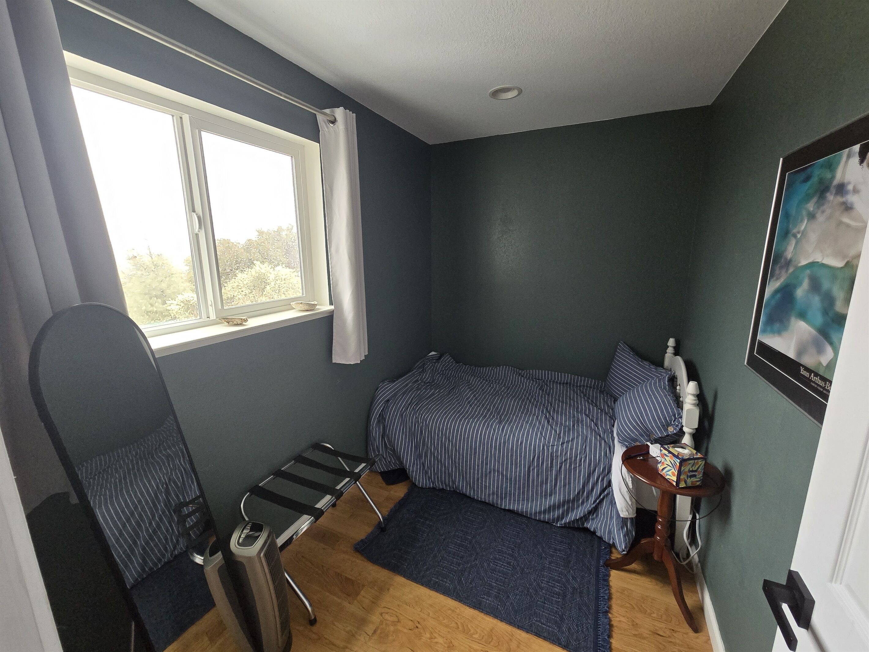 Une petite chambre à coucher, bien rangée, avec un lit simple, une chaise, une petite table et une fenêtre avec des rideaux.