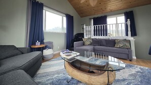 Ein Wohnzimmer mit Holzboden, einem grauen Sofa, einem blau gemusterten Teppich und einem einzigartigen Couchtisch in Bootsform.