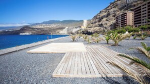A coastal hotel with a wooden deck, a rocky beach, and a view of the sea and mountains. - Home2Book Fantastic 160m2 Terrace Flat & BBQ (Radazul)