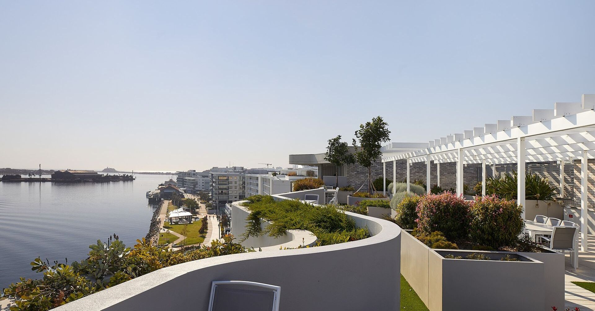 A waterfront property with a curved garden, outdoor seating, and a view of the water and cityscape.