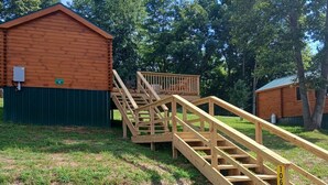 A wooden staircase leading to a cabin with a green roof, surrounded by grass and trees.