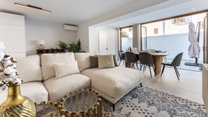 Un salon moderne avec un canapé d’angle, un coin repas comprenant une table et des chaises, et une vue sur l’extérieur.