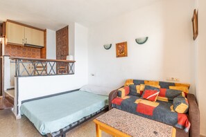 Um espaço compacto para viver, com cama, sofá, mesa pequena, cozinha e escada.