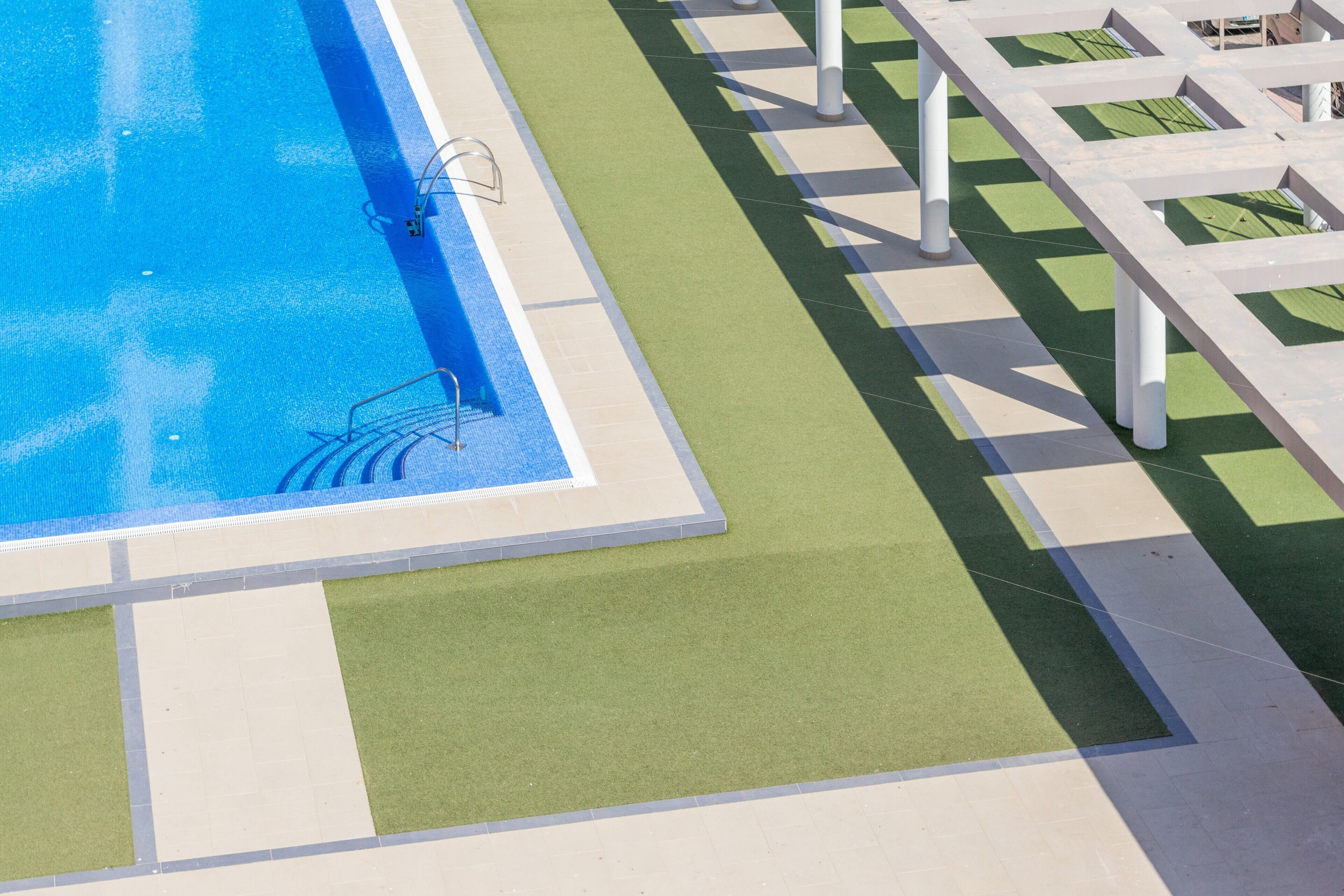 Ein Swimmingpool mit einer klaren, blauen Wasserfläche, umgeben von einer grün-beigen Fliesenveranda.