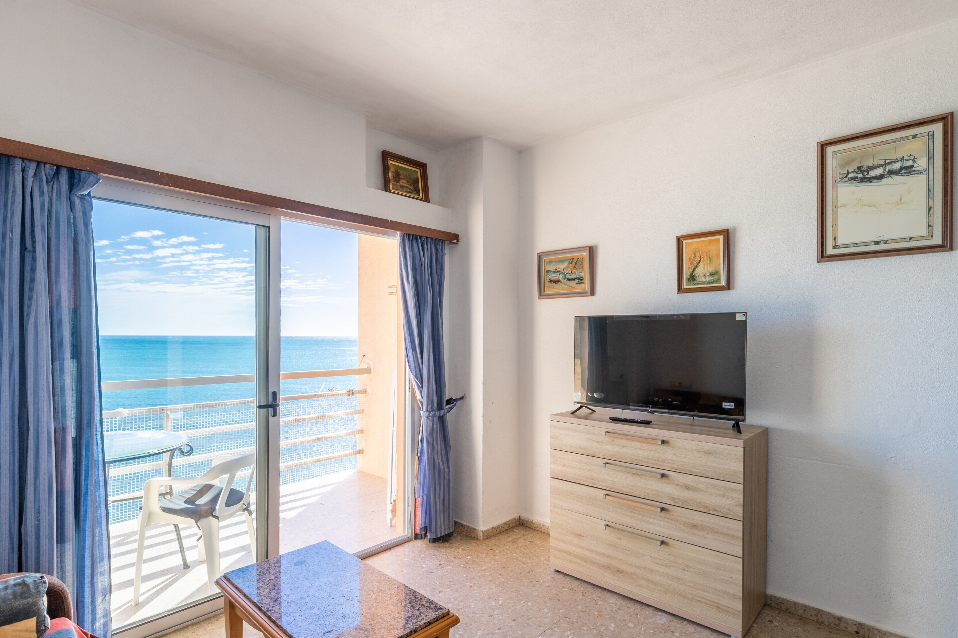 Une chambre dotée d’une télévision, d’une commode en bois et d’un balcon offrant une vue sur la mer.