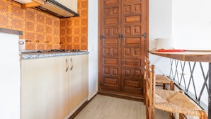 A kitchen with wooden cabinets, a double door, and a small dining table with chairs. - Studio Apartment 'Calpe Primera Linea' with Shared Pool, Balcony, and Wi-Fi (Calpe/Calp)