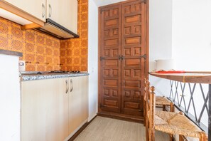 A kitchen with wooden cabinets, a double door, and a small dining table with chairs. - Studio Apartment 'Calpe Primera Linea' with Shared Pool, Balcony, and Wi-Fi (Calpe/Calp)