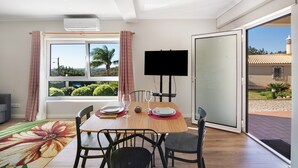 A dining area with a table set for two, a TV, and a view of the outdoors. - Holiday Home "Casa no Campo" with Sea View, Shared Pool and Wi-Fi (Loulé)
