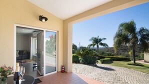 A room with a glass door leading to a patio, a table with a bottle and glasses, and a fire extinguisher. - Holiday Home "Casa no Campo" with Sea View, Shared Pool and Wi-Fi (Loulé)