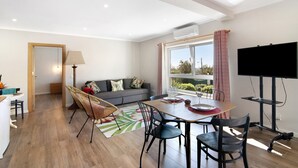 A modern living room with a dining area, a sofa, a TV, and a window with curtains. - Holiday Home "Casa no Campo" with Sea View, Shared Pool and Wi-Fi (Loulé)