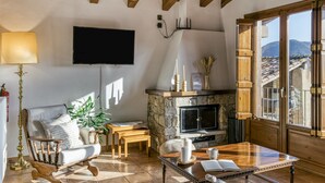 Un salon doté d’une cheminée en pierre, de meubles en bois, d’un téléviseur à écran plat et d’une grande fenêtre offrant une vue sur les montagnes.