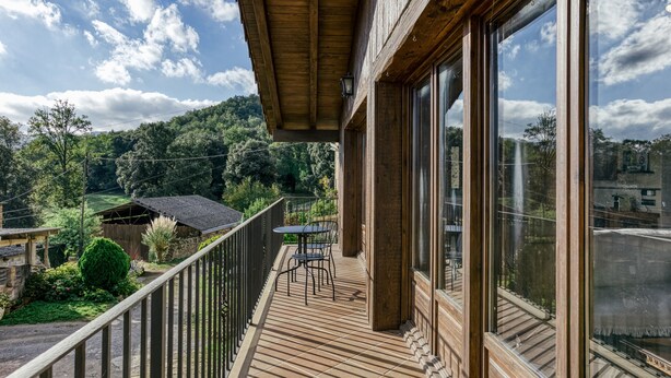 Une terrasse en bois avec une table et des chaises, donnant sur un jardin luxuriant et un paysage vallonné.