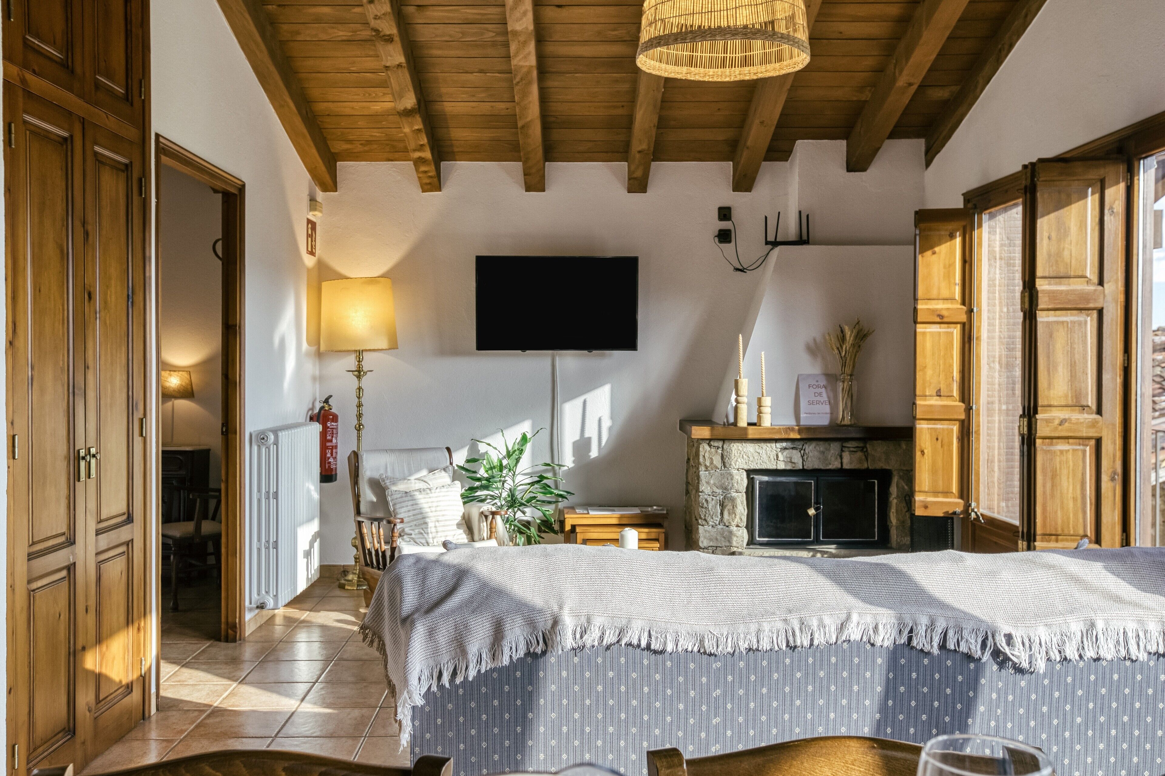 A bedroom with a bed, a television, a fireplace, wooden doors, and a hallway leading to another room.