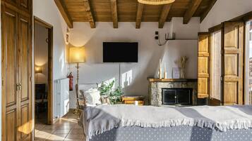 A bedroom with a bed, a television, a fireplace, wooden doors, and a hallway leading to another room.