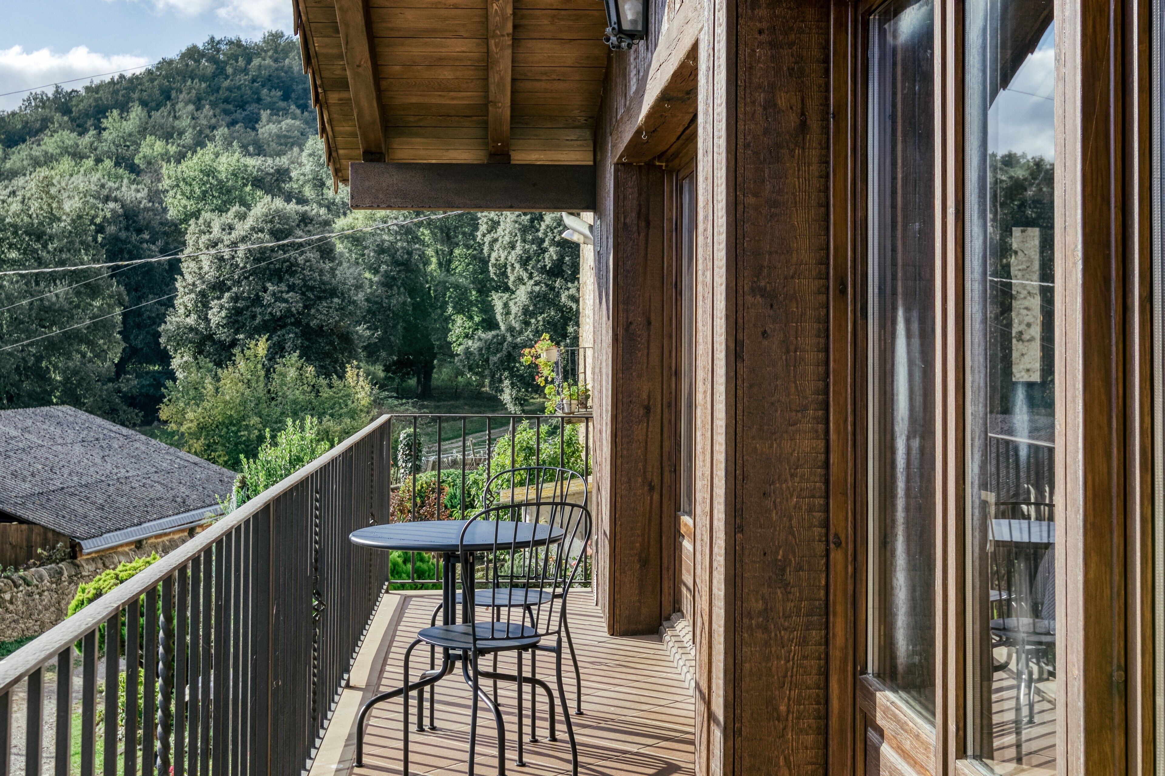 Una terraza de madera con mesa y sillas, con vistas a una ladera boscosa.