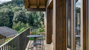 Una terraza de madera con mesa y sillas, con vistas a una ladera boscosa.