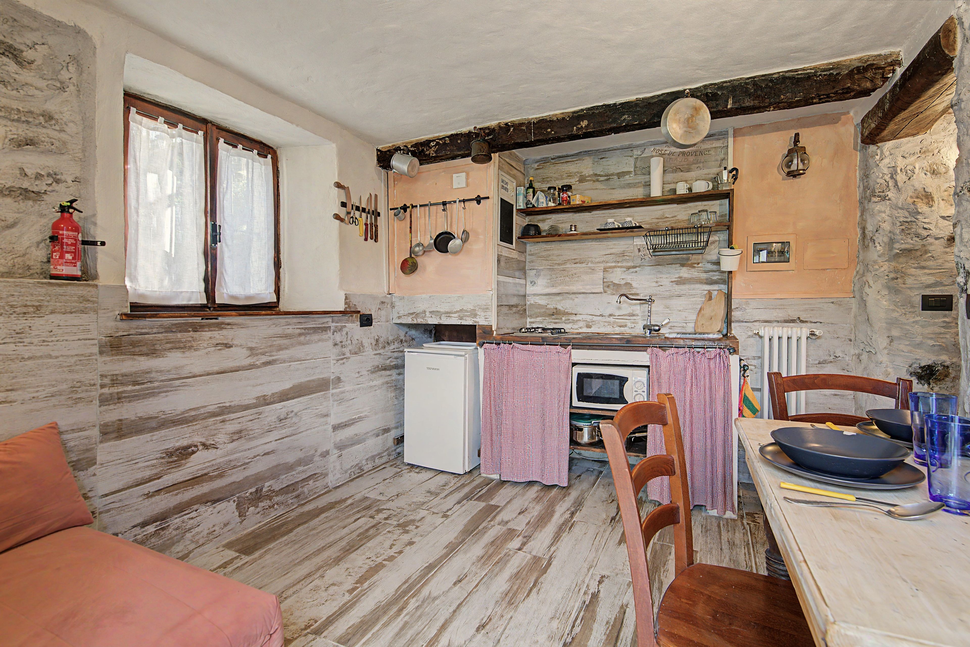 A rustic kitchen with a wooden floor, a white refrigerator, a stove, and a dining table with chairs.