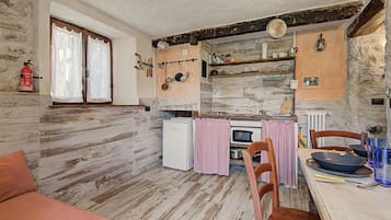 A rustic kitchen with a wooden floor, a white refrigerator, a stove, and a dining table with chairs.