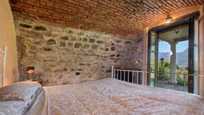 Un dormitorio con techo de ladrillo, una cama grande, una mesita de noche con lámpara y vistas a través de un ventanal.