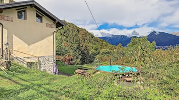 A house with a stone wall, a wooden deck, and a swimming pool surrounded by greenery.